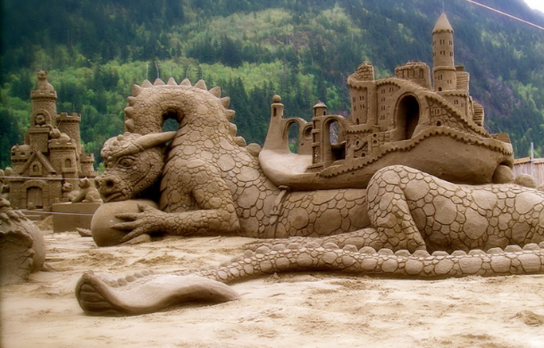 A sand sculpture of a dragon and a small castle.