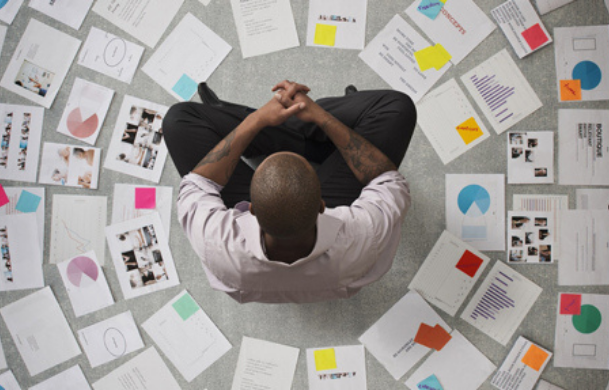 An overhead view of a man sitting on the floor surrounded by documents.